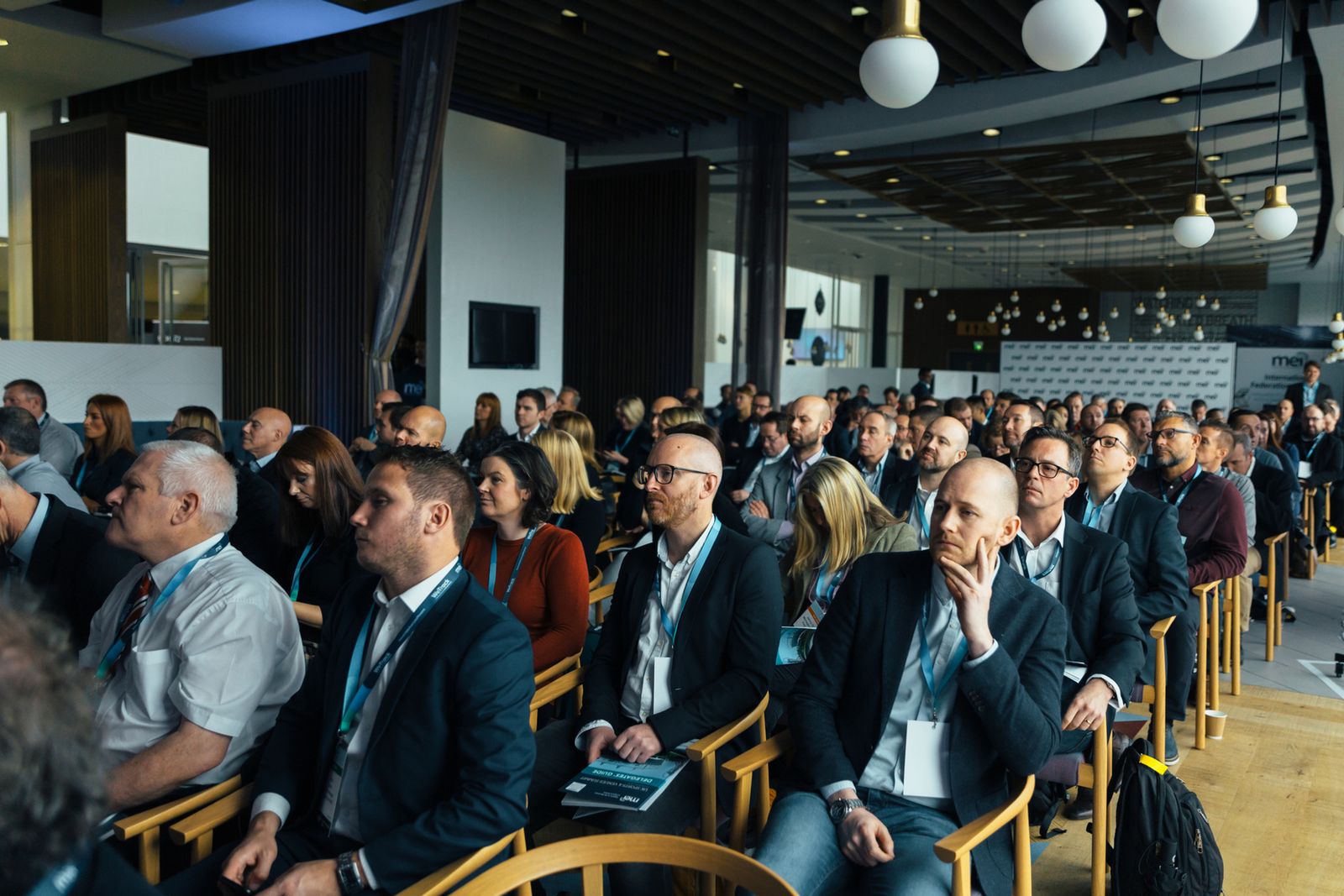 Delegates seated at a mid-size corporate conference, one holding a printed delegates guide booklet