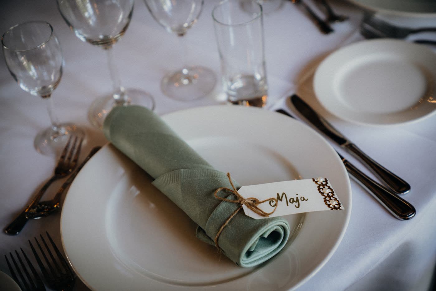A wedding place setting with a handwritten name tag tied to a folded napkin on a white plate